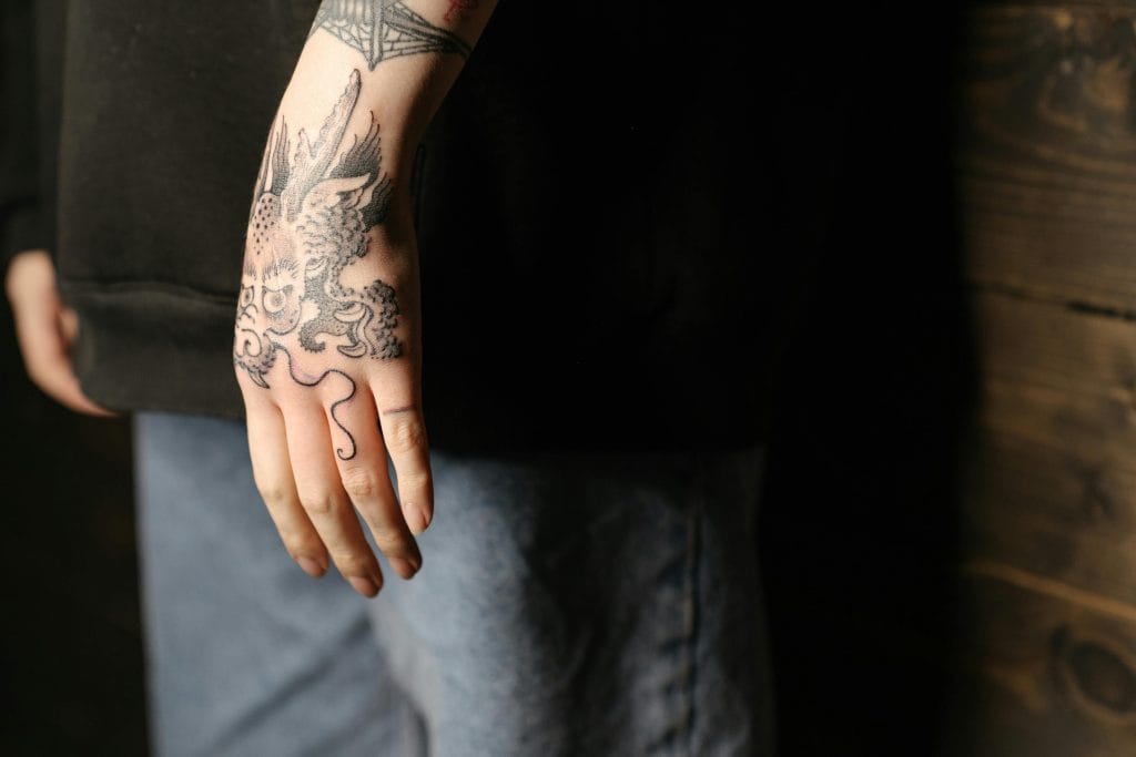 Detailed view of a dragon tattoo on a person's hand in an indoor setting.